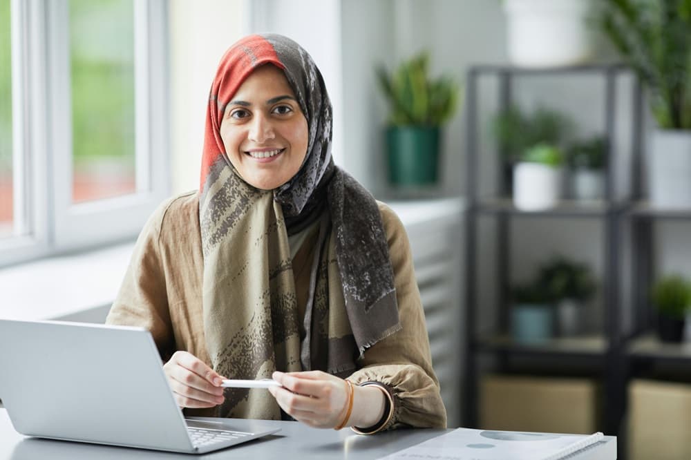 A volunteer in a hijab smiling at a laptop during the Express Volunteer Training cohort